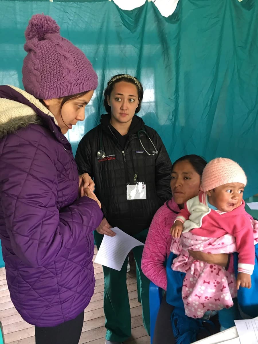 Clinicians examining a baby held by their mother