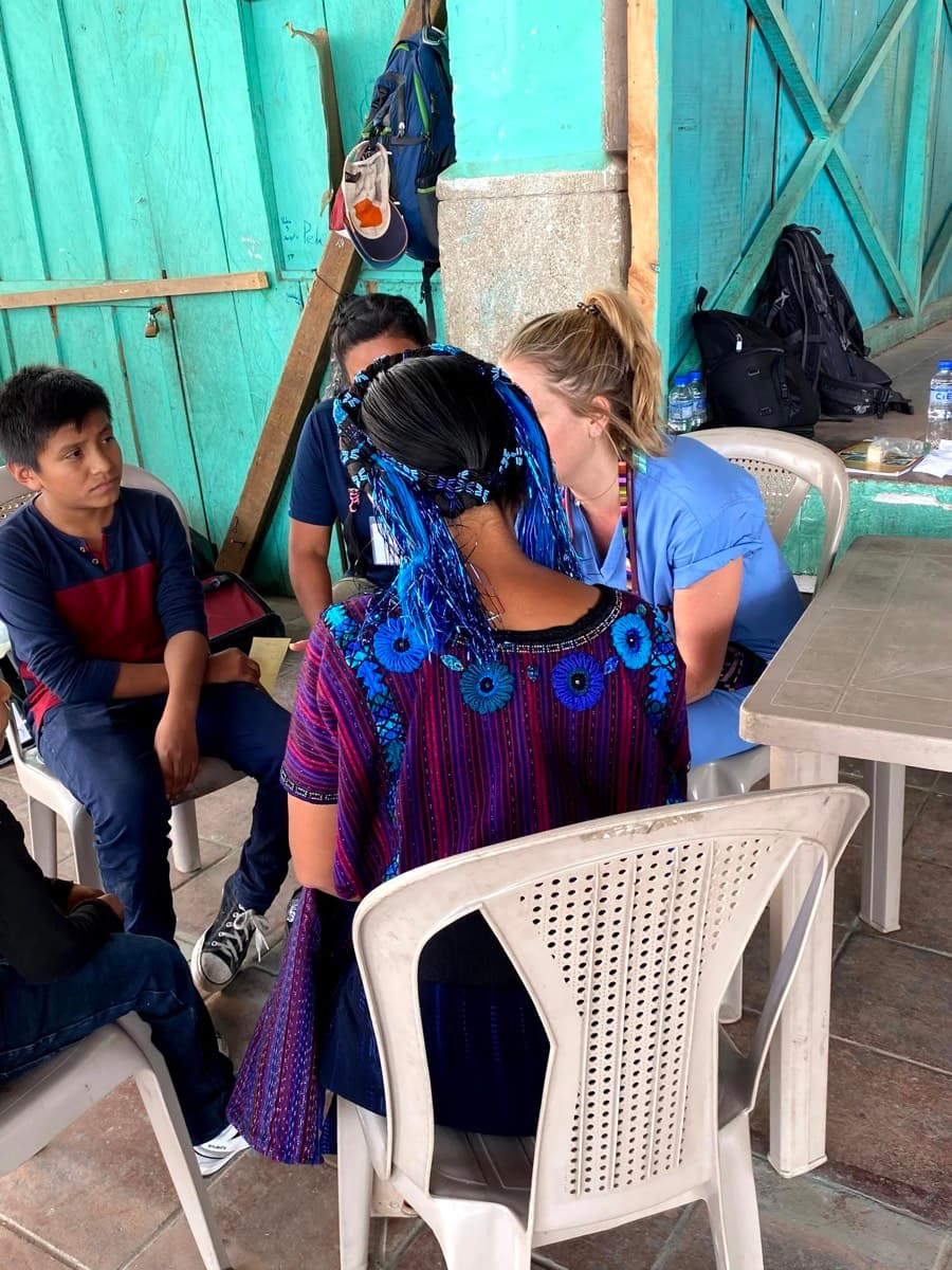 A volunteer sits with a woman in traditional Guatemalan dress during a clinic visit