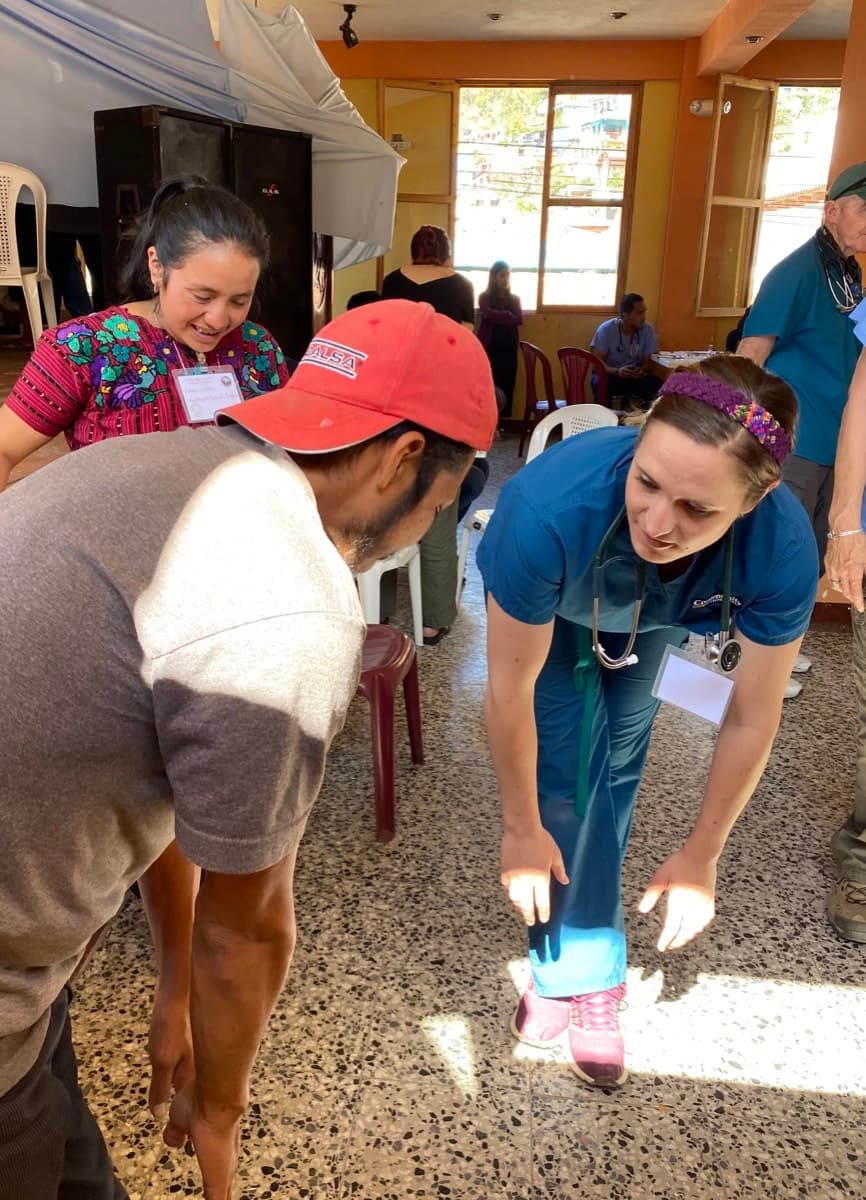 A volunteer in a red cap examines a patient at an outdoor clinic